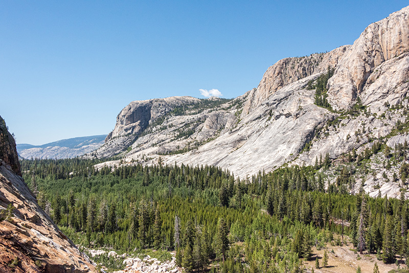 Green forested valley surrounded by exposed granite walls, with blue sky and one tiny cloud.